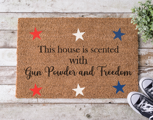 Coir doormat with bold lettering that reads ‘House is Scented with Gun Powder and Freedom,’ hand-painted in a rustic, patriotic style.