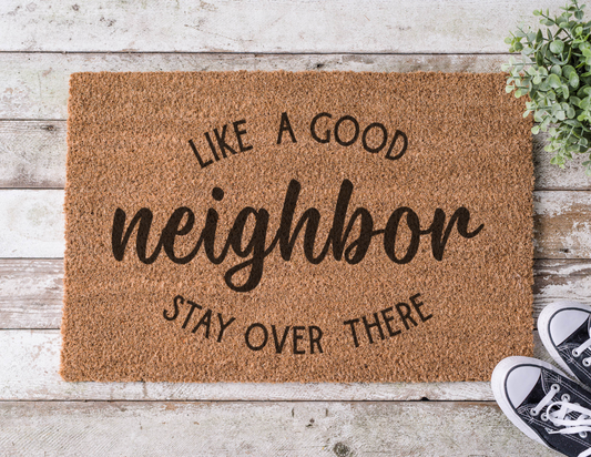 Coir doormat with the phrase ‘Like a Good Neighbor, Stay Over There,’ hand-painted in bold, humorous lettering