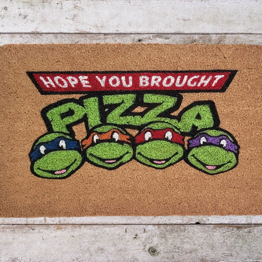 Coir doormat with the phrase ‘Hope You Brought Pizza,’ hand-painted in bold, playful lettering with a Ninja Turtle–inspired design