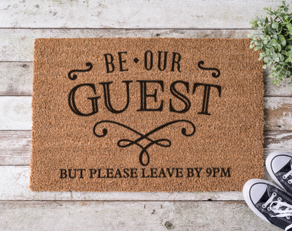Coir doormat with the phrase ‘Be Our Guest but Leave by 9,’ hand-painted in bold, playful lettering for introverts and early sleepers