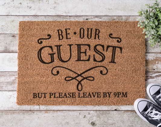 Coir doormat with the phrase ‘Be Our Guest but Leave by 9,’ hand-painted in bold, playful lettering for introverts and early sleepers