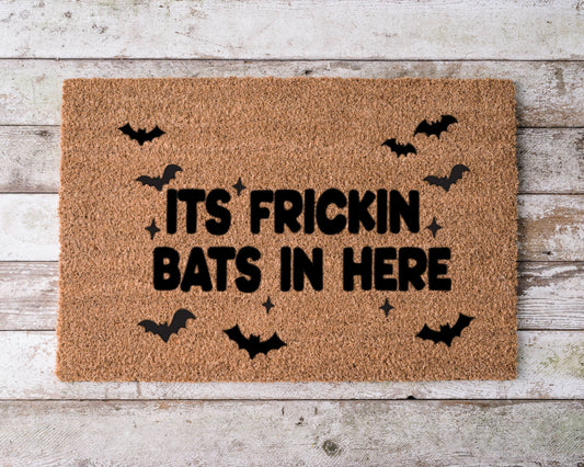 Doormat with the phrase “It’s Frickin Bats in Here” and hand-painted flying bat illustrations – funny Halloween porch decor.