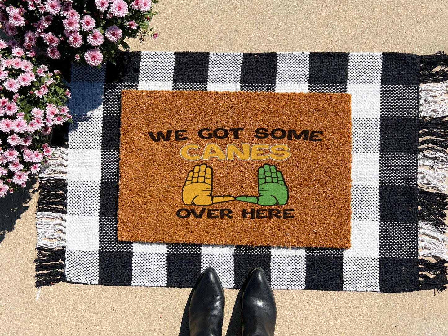 Doormat with 'We Got Some Canes Over Here' text and hand graphics on a checkered mat with boots and flowers.