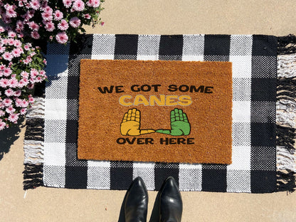 Doormat with 'We Got Some Canes Over Here' text and hand graphics on a checkered mat with boots and flowers.